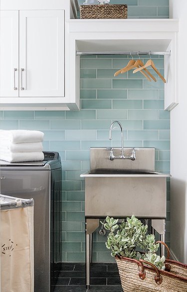 Laundry room with teal subway tile and a freestanding stainless steel sink.