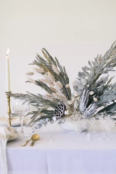 Glittery dried flowers and grass painted gray on table with candles and dishware
