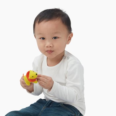 little kid with white shirt holding yellow and orange toy lion