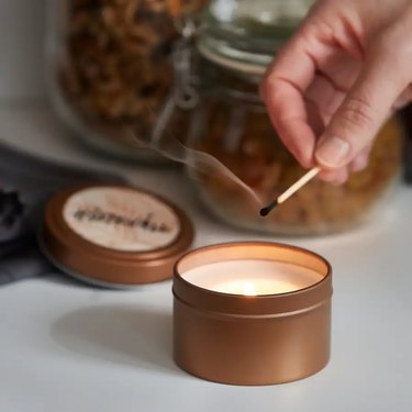 person holding match over candle in tin