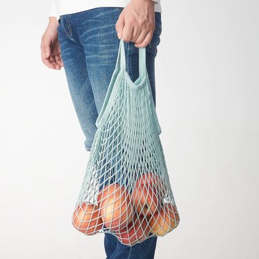 person in jeans holding mesh bag with apples inside them