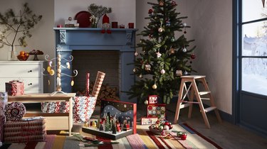 A living room featuring a Christmas tree, light blue fireplace, and toys and wrapping paper on the floor.