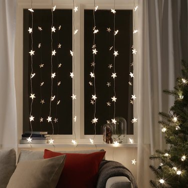 Star-shaped string lights covered a window like a curtain next to a Christmas tree.