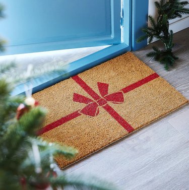 A brown door mat that looks like it has been wrapped with a red bow.