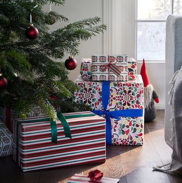 Three packages in assorted gift wrap under a Christmas tree with red bulb ornaments.
