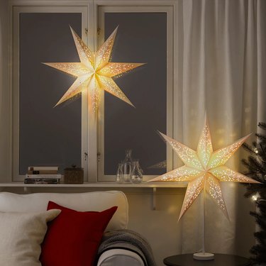 Two seven-pointed star lampshades that glow from within hung in a living room above a white couch.