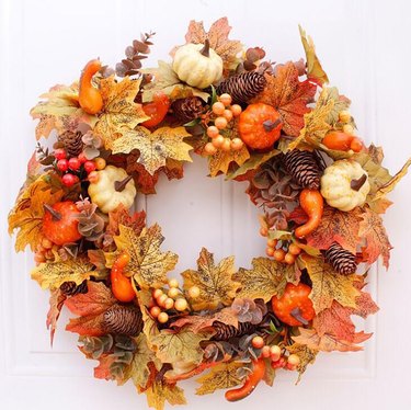 A wreath on a front door with autumn leaves small pumpkins and pinecones