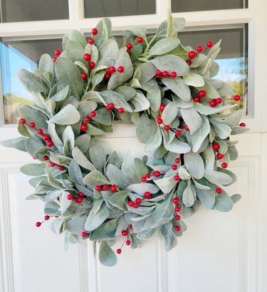 A lambs ear wreath with red berries on a white door