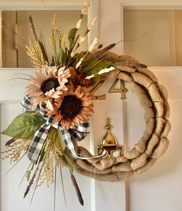 A burlap wreath with flowers straw and leaves on one side