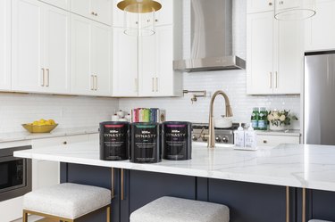 White kitchen with marble top island and 3 Behr paint cans on the counter