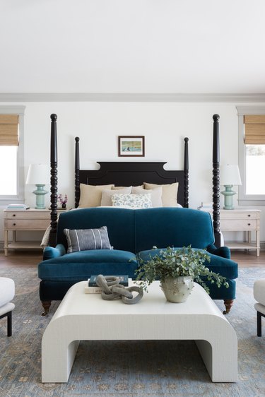 bedroom with black four-poster bed and teal couch and white coffee table seating area in front of it