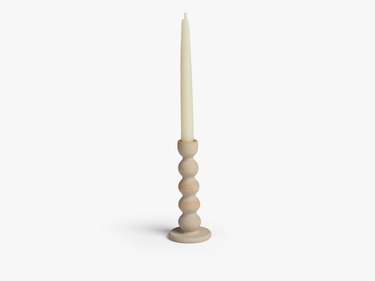 A wavy speckled, unglazed candlestick with a white taper candle in it.