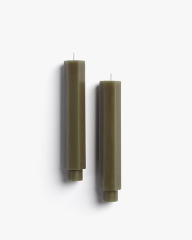Two moss-colored taper candles on a white background.