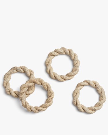 Four twisted, circular napkin holders in a beige speckled clay.