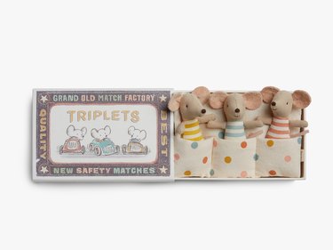 A matchbox that opens up to reveal three mini stuffed mice toys in blue, yellow, and red striped shirts.