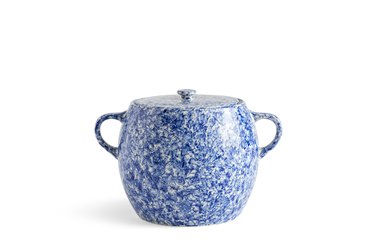A blue and white speckled bean pot with a lid and two handles over a white background.