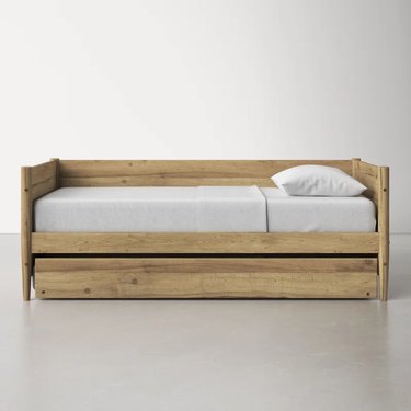 A light wood trundle bed with a white mattress and white pillow on top.
