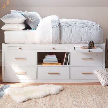 A white captain's bed with a mattress on top and six large drawers beneath it.