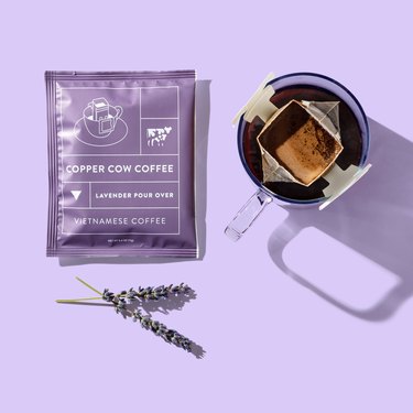 purple package that reads "copper cow coffee" near lavender and coffee filter on mug