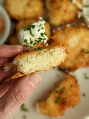 Hand holding a piece of a thick and crispy potato latke over a plate of other latkes.
