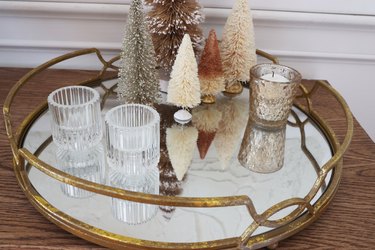 Fluted glass and mercury glass votive holders placed on mirrored tray next to bottle brush trees
