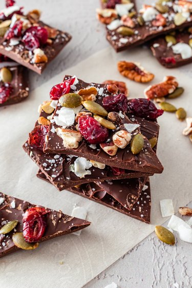 A piece of chocolate bark topped with cranberries, pepitas, pecans, coconut flakes, and sea salt.