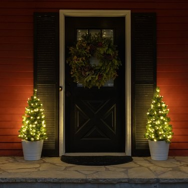 A front porch with two small evergreen trees that are lit