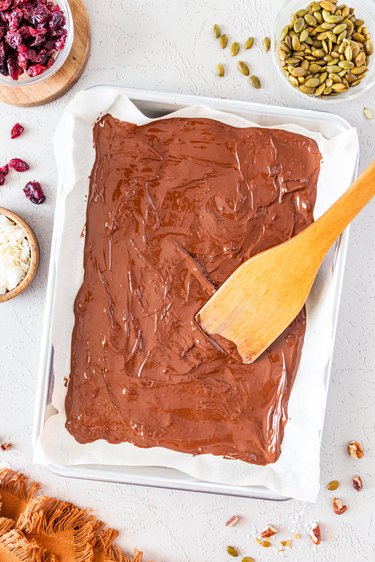 The melted dark chocolate spread out on an aluminum baking sheet topped with parchment paper.