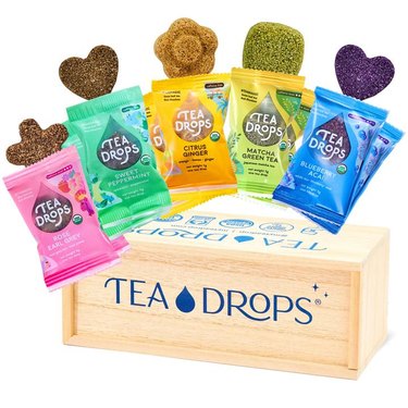 five packets of tea with different shapes and a wood box that reads "tea drops"