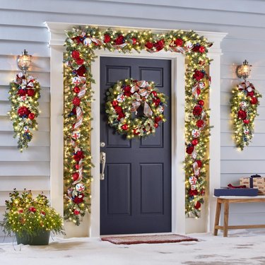 A front porch decorated for Christmas with a lit garland and wreath