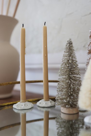 Two yellow taper candles placed on mirrored tray next to gold bottle brush tree