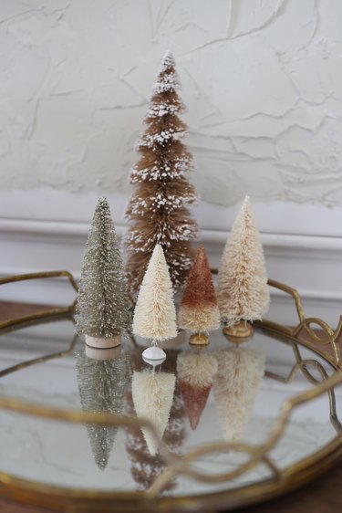 Five sparkly metallic bottle brush trees placed together on mirrored tray