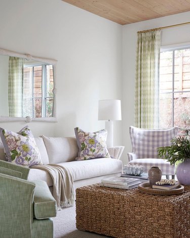Living room with white walls and sofa and lavender and pastel green accent chairs, pillows and curtains.