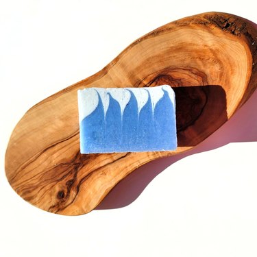 A bar of blue and light blue blueberry soap on a block of wood.