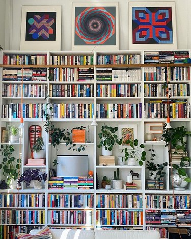 A white living room with high ceilings and a large window with a bookshelf that goes almost to the ceiling.