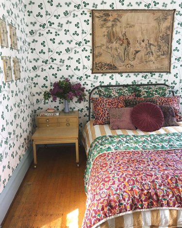 Bedroom with green clover wallpaper, floral and striped bedding in burgundy, green and mustard yellow.