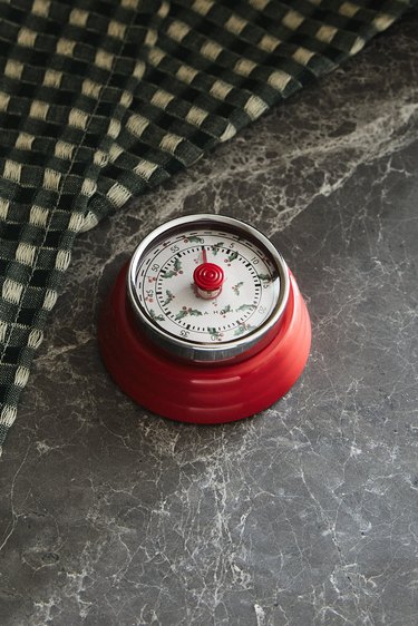 A red kitchen timer with holly illustrations on the white clock face.