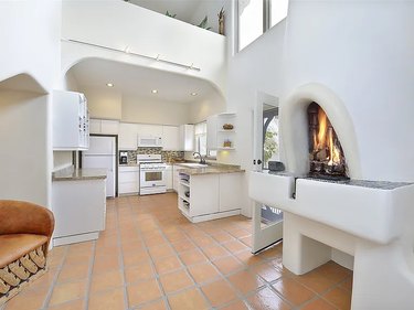 A white interior kitchen with arched ceilings and doorways, and a brown-tiled floor.