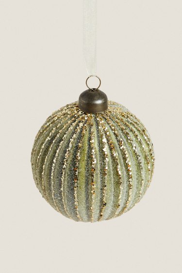 A light green Christmas ornament with gold glitter vertical lines across it.