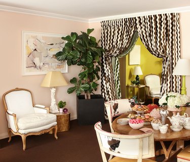 Dining room with traditional furnishings, blush walls, chocolate brown and white zigzag striped curtain, and a peek of a chartreuse wall beyond.