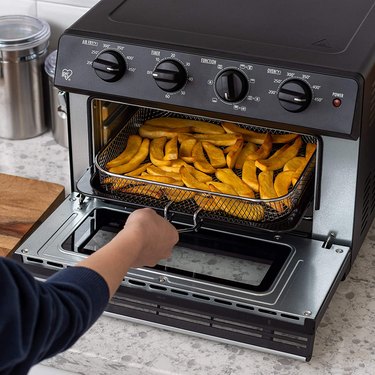 person reaching into black air fryer for fried potatoes