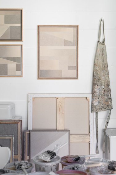 Canvases with neutral geometric shapes hanging on a white wall next to a paint smock