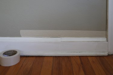 Attaching white painter's tape along bottom edge of wall