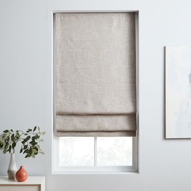 A neutral colored Roman shade is hung in a window