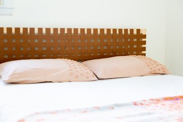 Bed with beige pillows and a wood frame headboard with faux leather strips forming a weave pattern