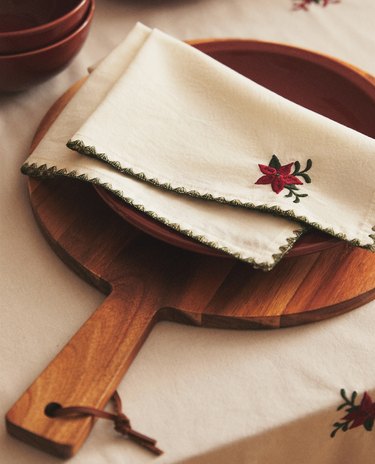 a round wood board with a white napkin with a red embroidered flower