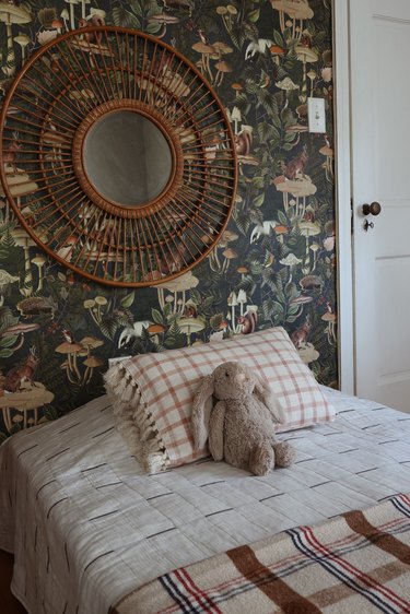 Removable green forest animal wallpaper in kids room with plaid bedding and wicker mirror