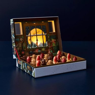An open box of chocolates shaped like Santa on a navy blue background.