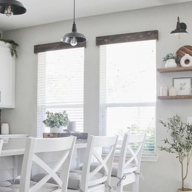 Wooden farmhouse cornices are hung on two windows in a white kitchen