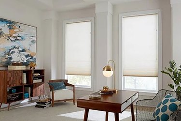 A living room with two windows that are covered in cellular shades
